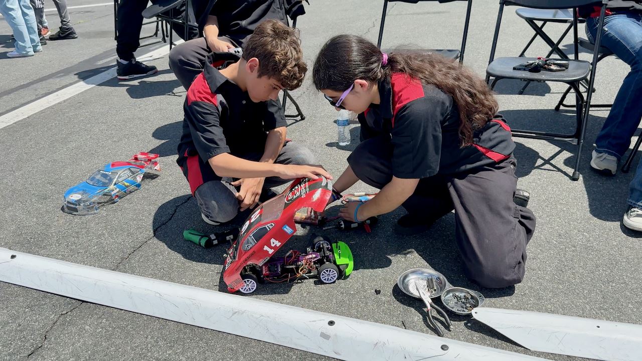  Two sudents work on radio controlled car's engine and components